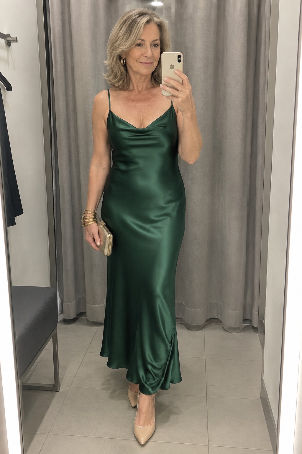 Woman in long emerald satin slip dress taking mirror selfie in fitting room