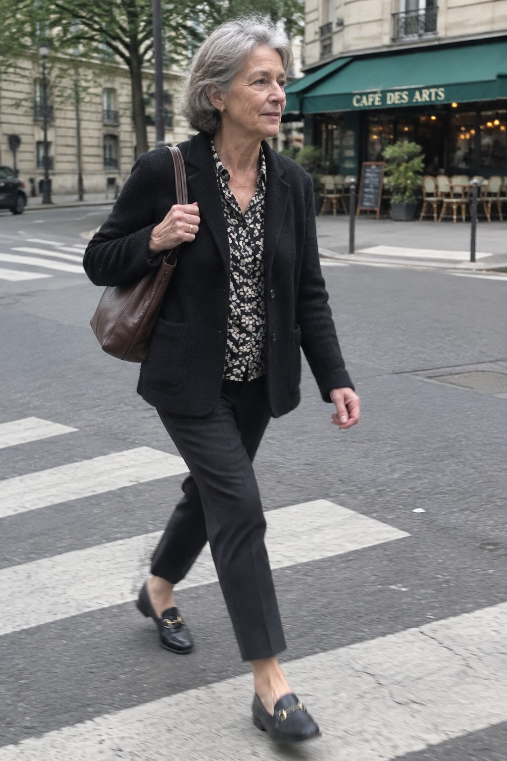 Gray-haired woman in black jacket crossing street with brown leather bag near cafe